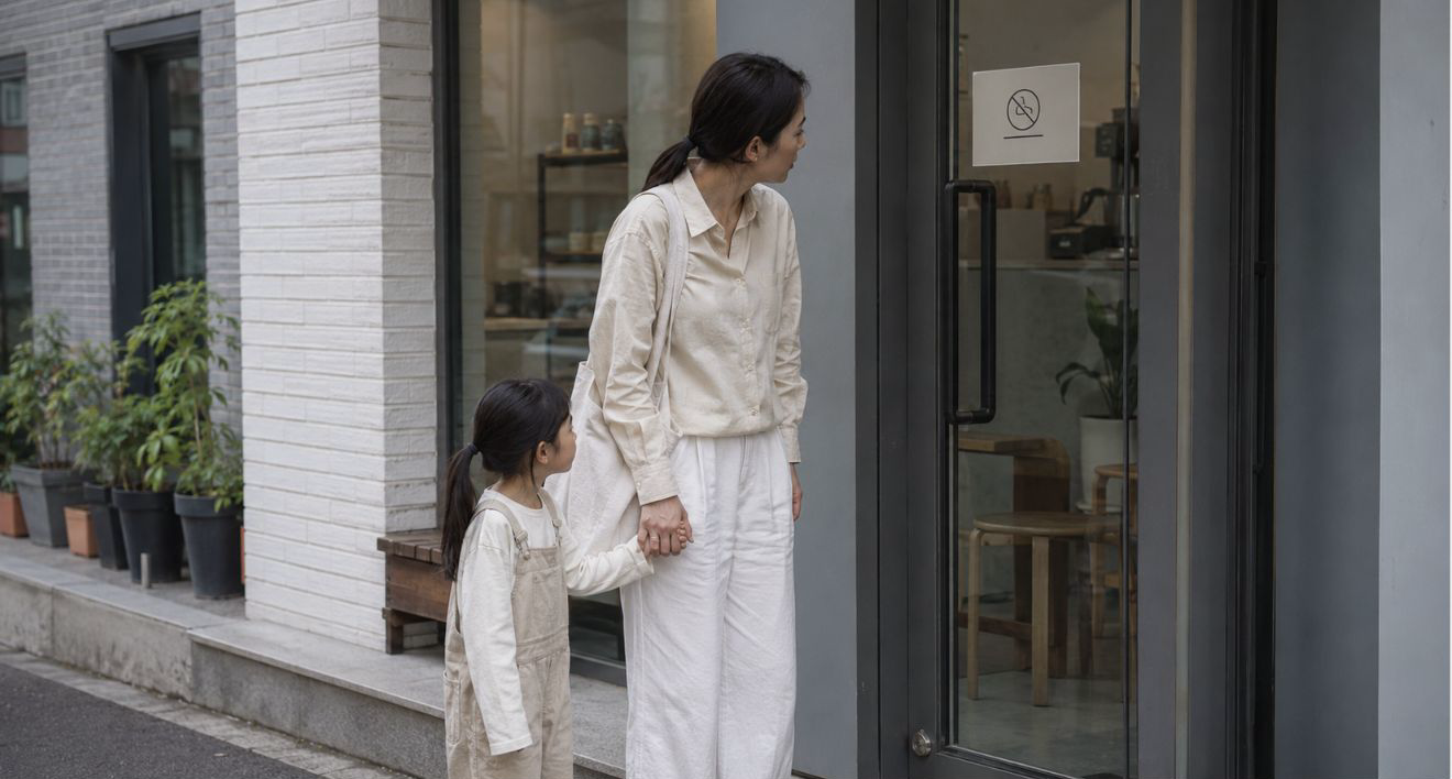 카페 입구 앞에서 아이 손을 잡은 부모가 노키즈존 안내문을 바라보는 장면